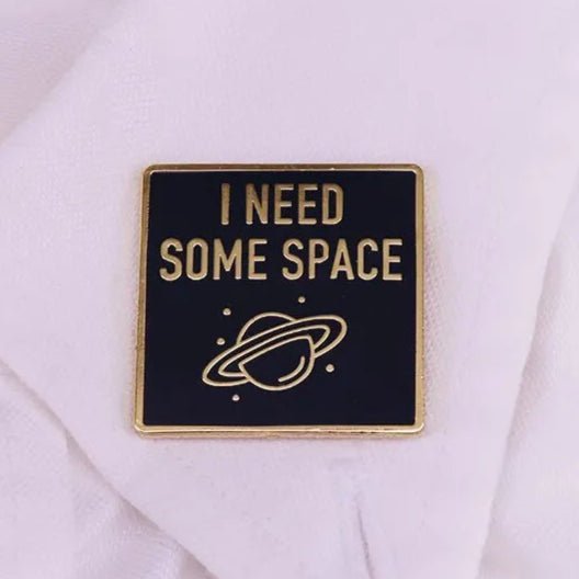 A square black and gold metal brooch by Kiss Me Later reads “I NEED SOME SPACE” above a planet with rings—an on-trend star pin perfect for any unisex accessory collection.