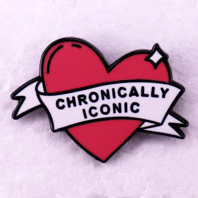 Enamel pin featuring a pink love heart and a white banner with CHRONICALLY ICONIC in bold black letters, set on a light pink background.