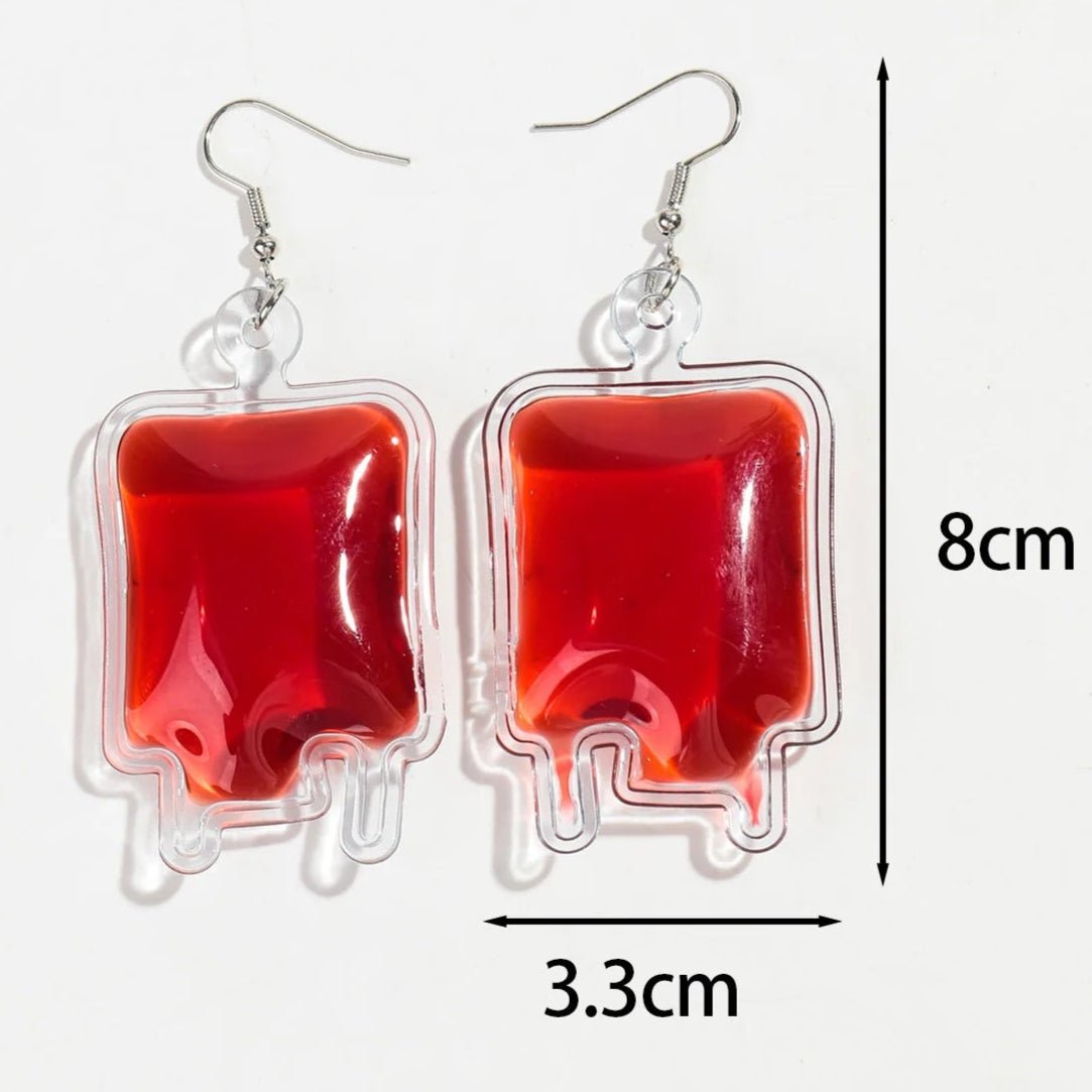 Kiss Me Later gothic blood bag earrings, filled with red liquid and measuring 8 cm by 3.3 cm, are shown against a white background.