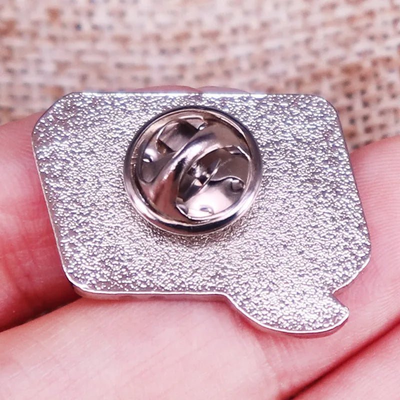 A close-up shows a hand holding the retro speech bubble silver metal pin with a textured back and butterfly clutch. Burlap fabric is blurred in the background. Ships worldwide.