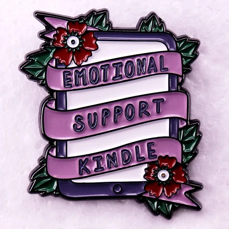 Enamel pin features an e-reader wrapped in a pink ribbon reading EMOTIONAL SUPPORT KINDLE, decorated with red flowers and green leaves—a cute accessory for romance readers and book lovers.