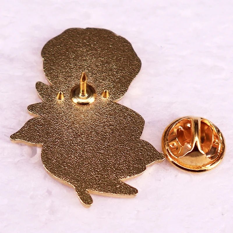 gold enamel flower pin with leaf accents is shown facedown beside its butterfly clutch backing on a white surface.