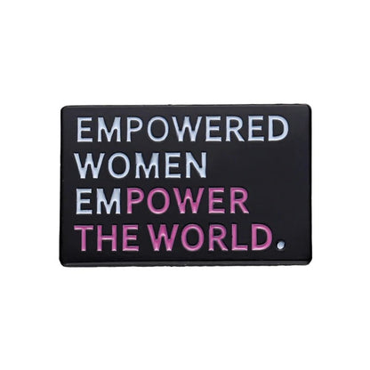 A rectangular black enamel pin features “Empowered women empower the world” in white and pink capitals—a bold statement piece for any feminist pin collection.