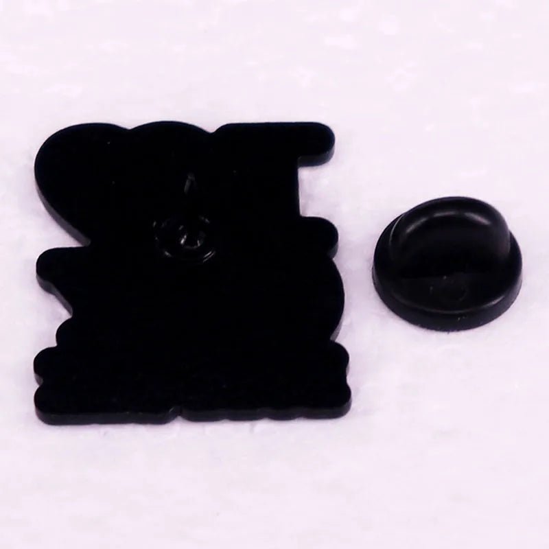 The Kiss Me Later black enamel pin features a rounded, heart-like silhouette. It comes with a separate black rubber clutch back and is displayed on a light, textured surface.