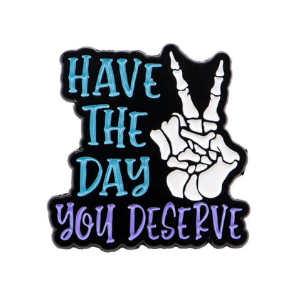The image displays the text Have the day you deserve in teal and purple beside a skeleton hand peace sign pin on a black background. 