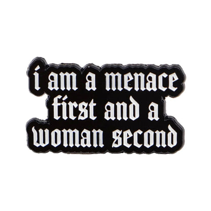 A black enamel pin features white Gothic text: i am a menace first and a woman second, and is accented with a bold red heart for extra attitude.