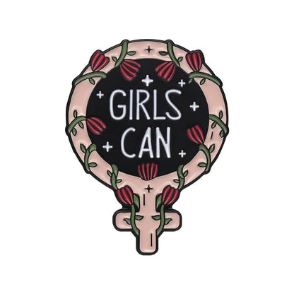 enamel pin features a stylized Venus symbol with tulip flowers, vines, a love heart, and GIRLS CAN in white on a black background inside the circle.