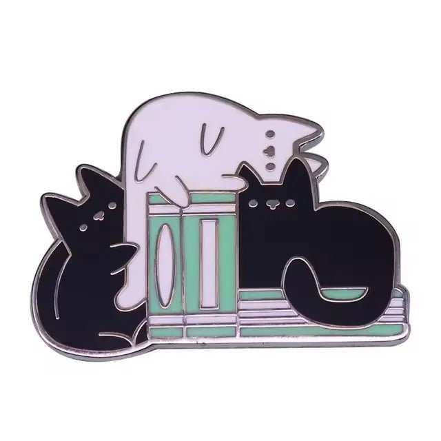 The My Cutesy Era enamel pin features two black cats and a white cat lounging on green and teal books—a perfect accessory for book lovers and cat enthusiasts alike.