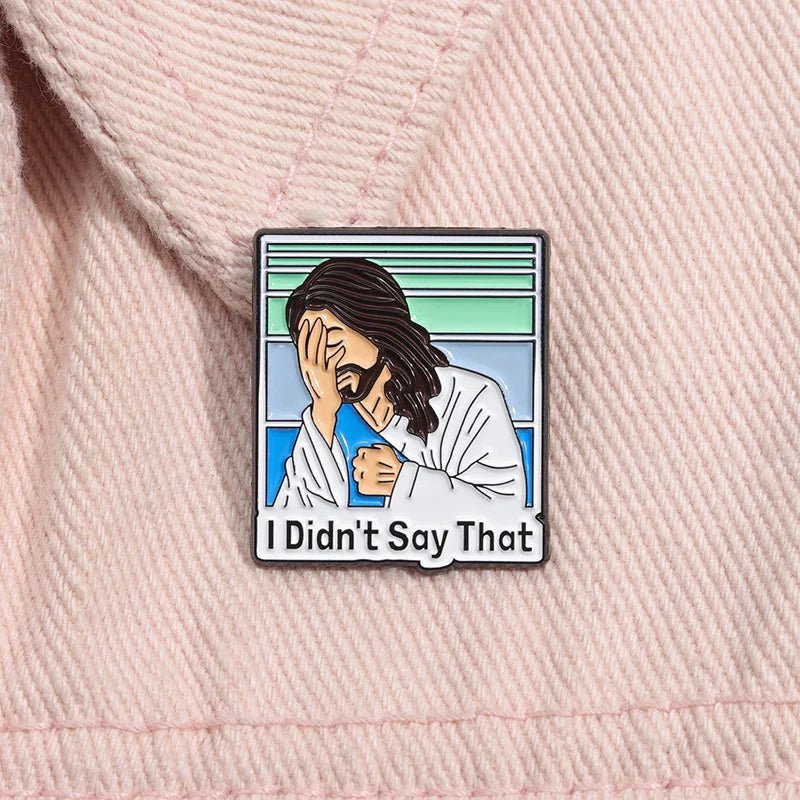 Bible-themed pin shows a cartoon Jesus facepalming in a white robe on pastel stripes with “I Didn’t Say That” text. This funny pin is displayed on light pink fabric.