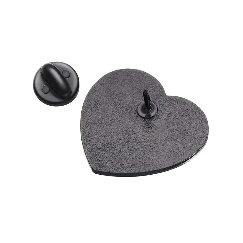 Back metal heart enamel pin with a textured surface is displayed, its round backing set beside it. The sharp central post is visible, showing the detailed craftsmanship of this stylish accessory.