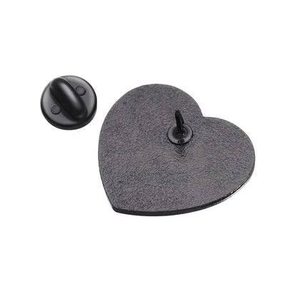 Back metal heart enamel pin with a textured surface is displayed, its round backing set beside it. The sharp central post is visible, showing the detailed craftsmanship of this stylish accessory.