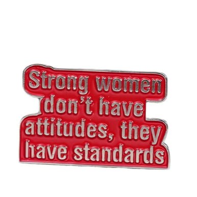 A red enamel pin by My Cutesy Era features white text: Strong women don’t have attitudes, they have standards—a striking accessory for those who support feminism and empower strong women.