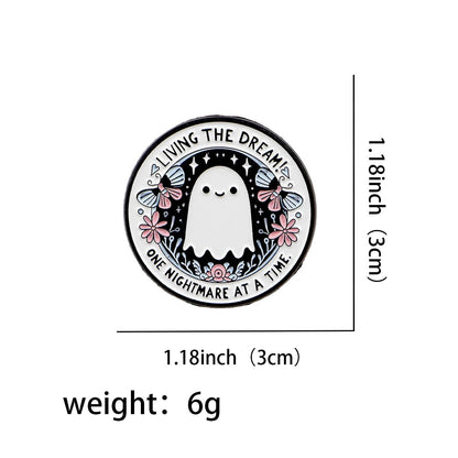 A round pin features a cute ghost with stars, flowers, and butterflies. Text says Living the dream, one nightmare at a time. The pin measures 1.18 inches (3 cm) wide and weighs 6 grams.