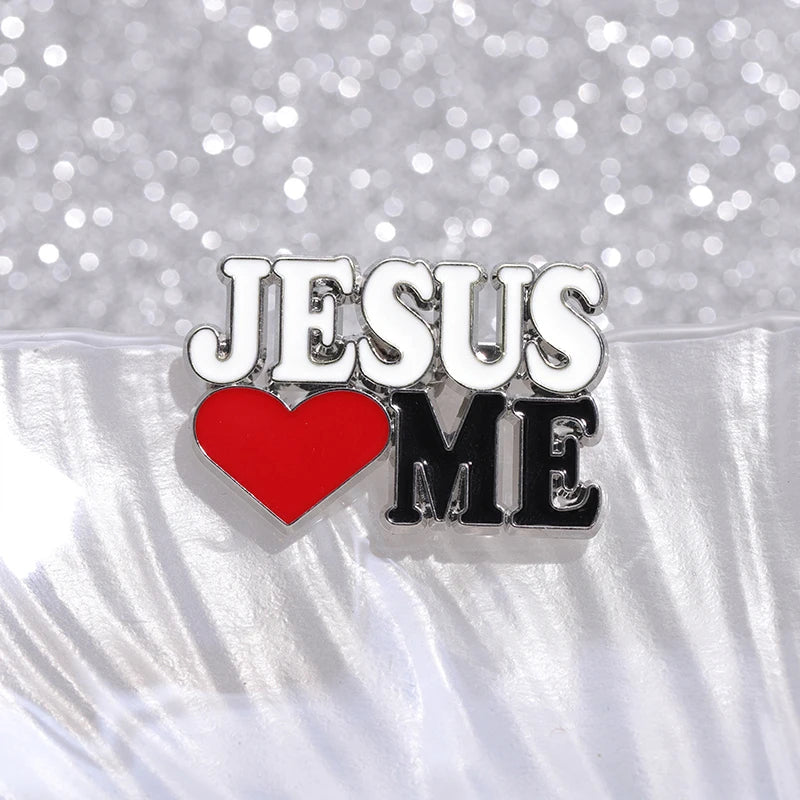 A cute pink enamel pin by Kiss Me Later, featuring JESUS ♥ ME with a red heart symbol for loves, displayed on a shiny, textured background.