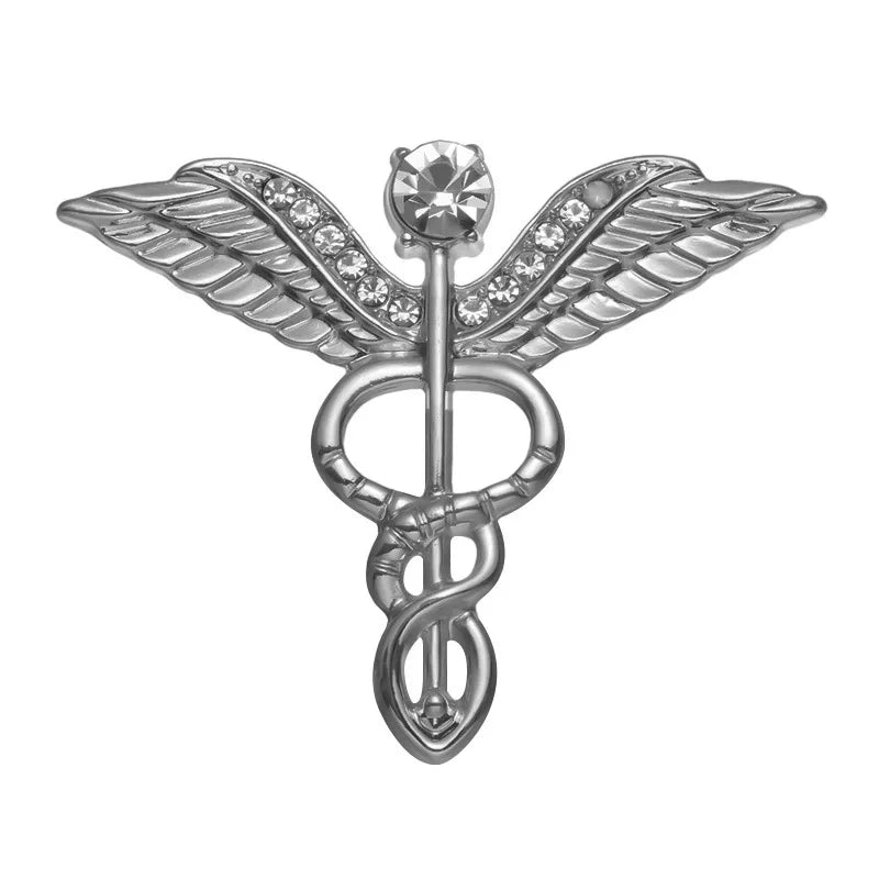 A unique silver medical symbol pin with two wings, a rod, and entwined snakes, adorned with rhinestones and a prominent jewel—an ideal feminist gift for any occasion.