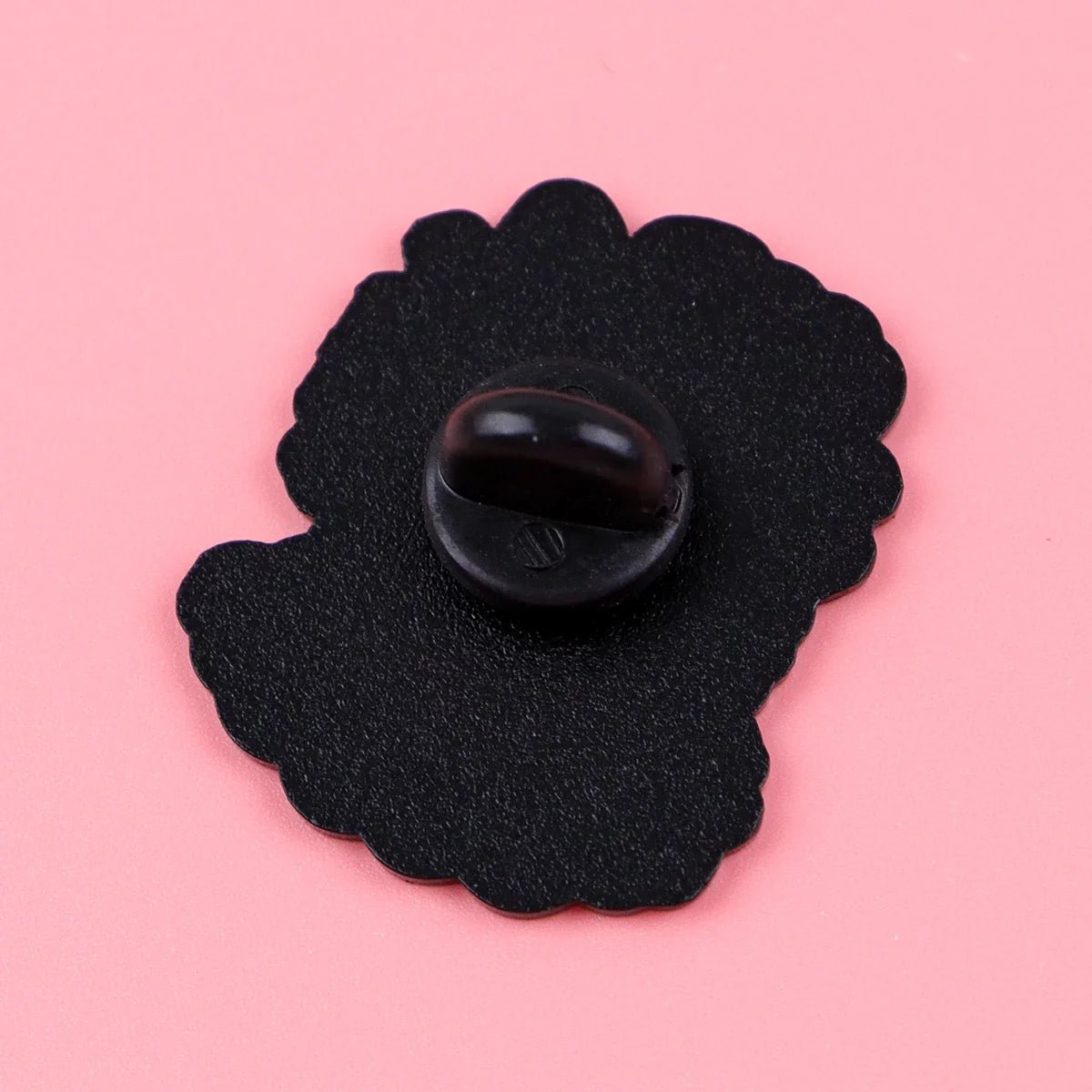 A wavy-edged black enamel pin backing with a rubber clutch from Gay Skate rests on a pink background—a perfect addition to your pride accessories collection.