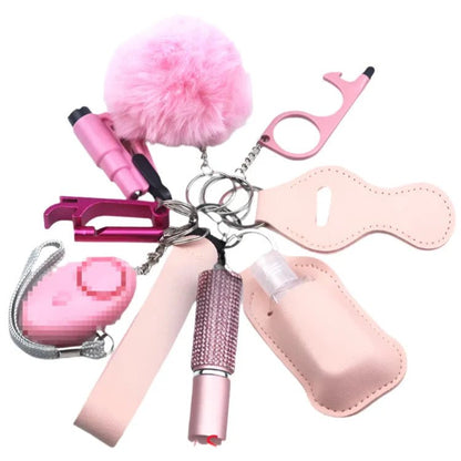 The Kiss Me Later set features pink personal safety essentials—a pom-pom, safety alarm, whistle, no-touch tool, and glittery pepper spray holder—all on a keyring, ideal for outdoor activities or everyday use.