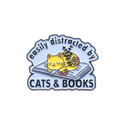 My Cutesy Era’s book pin shows a yellow cat napping on an open book beside a potted plant. With “easily distracted by CATS & BOOKS” text, it’s a perfect gift or accessory for book lovers and bookworms.
