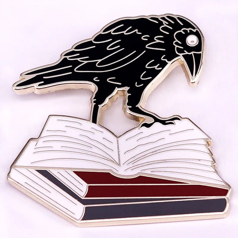 An enamel pin featuring a black raven atop an open book with visible pages and a red-bordered cover—an ideal unique badge for romance readers and book lovers.