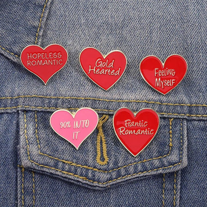 Five heart-shaped red and gold enamel pins featuring phrases like Hopeless Romantic and Gold Hearted, add a playful pop of color to a blue denim jacket pocket.