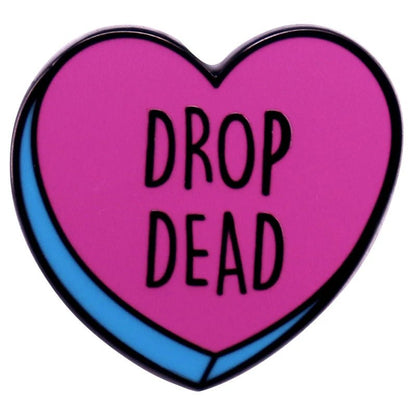 The Kiss Me Later pink and blue enamel love heart pin features a bold blue border and DROP DEAD in striking black letters at the center.