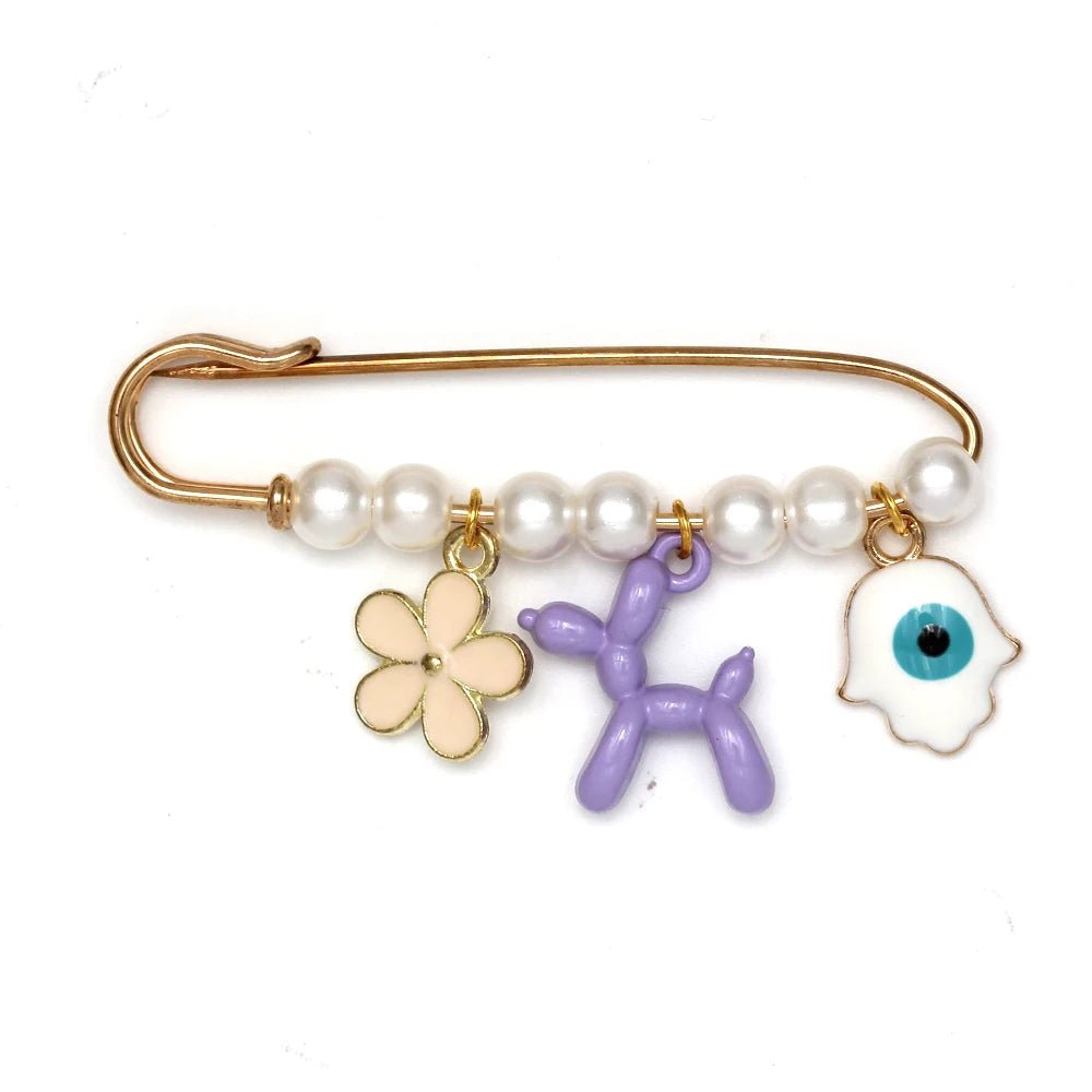 The Kiss Me Later gold evil eye pin features five pearl-like beads and three dangling charms—a pink flower, purple balloon dog, and white hamsa hand—creating a delightful brooch thats perfect as a baby shower gift.