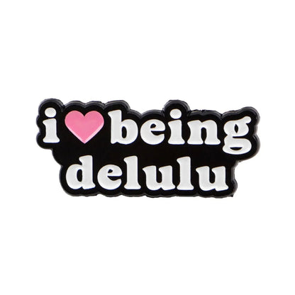 pin with i ♥ being delulu in white on black, the word love as a red heart enamel accent.