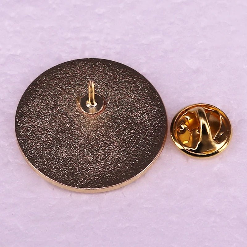 Round metallic pin-back badge, echoing white and gold enamel, lies face down beside its gold-toned butterfly clutch on a light textured surface.