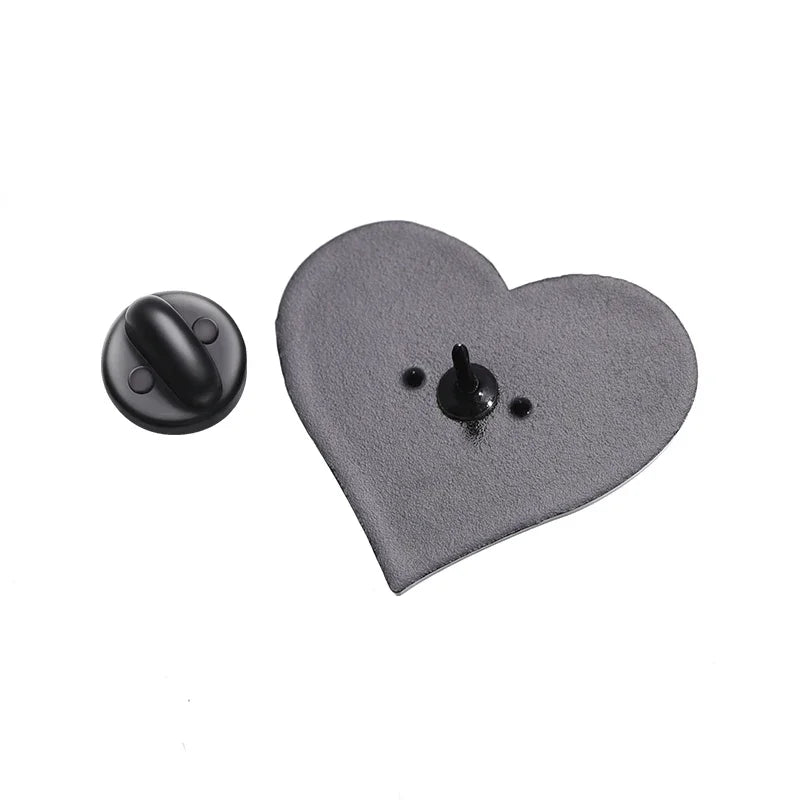 Gothic black metal heart-shaped pin badge with a sharp center post, displayed beside its round black clutch backing on a white background.