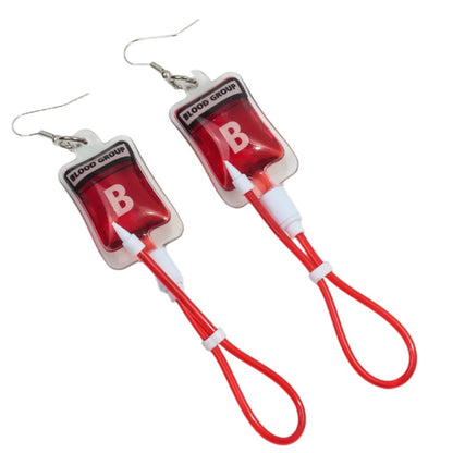 Kiss Me Later presents blood bag earrings shaped like blood group B bags, with red tubing, clear plastic, and metal hooks—ideal for nurses or anyone wanting a quirky gothic accessory.