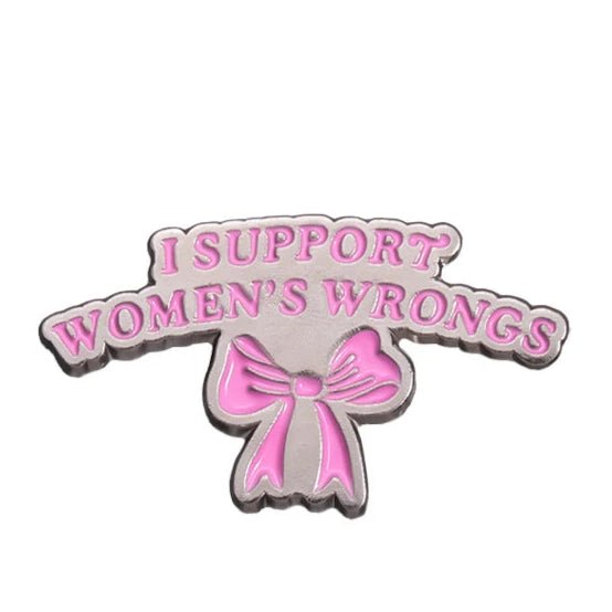 A silver enamel pin by My Cutesy Era features pink I SUPPORT WOMENS WRONGS text above a pink bow on a white background—a bold accessory celebrating feminism and strong women.
