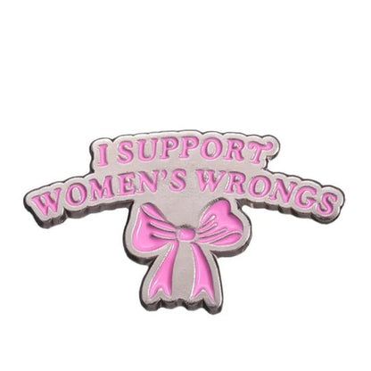 A silver enamel pin by My Cutesy Era features pink I SUPPORT WOMENS WRONGS text above a pink bow on a white background—a bold accessory celebrating feminism and strong women.