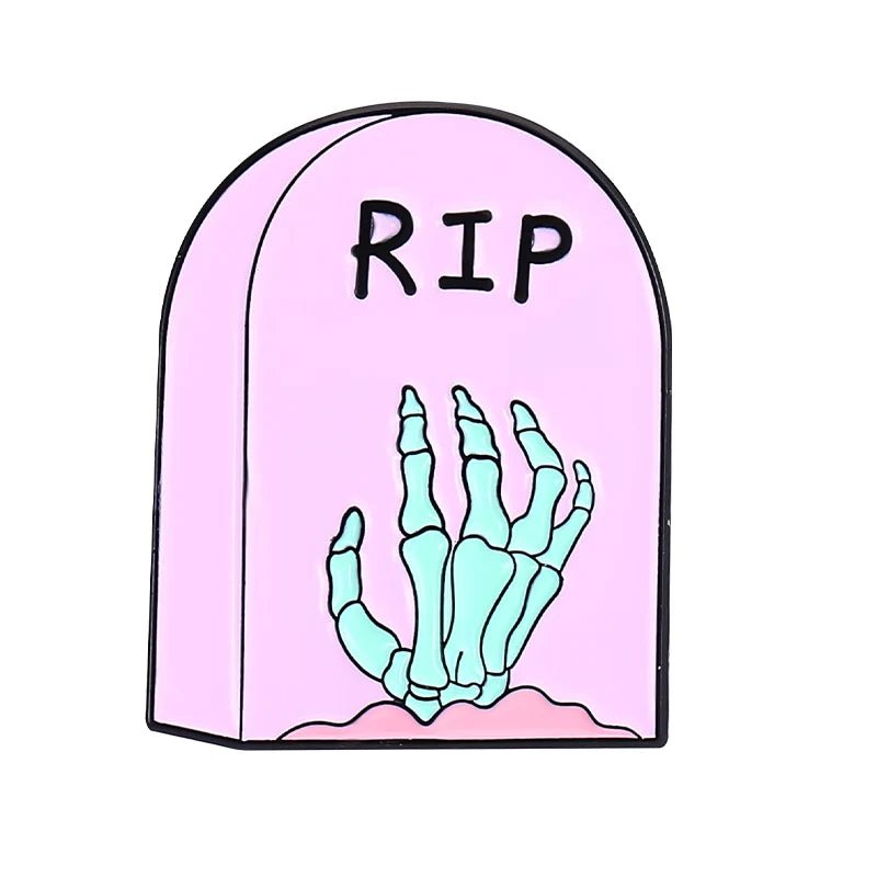 A pink tombstone enamel pin with RIP and a turquoise skeleton hand emerging from the base—perfect to pair with your favorite skull enamel pin.