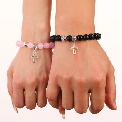 Two hands wear Kiss Me Later crystal bead bracelets: pink on the left and black on the right, each with a silver cross charm—stylish Christian stone bracelets for expressing your faith.