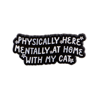 black enamel pin features white text, “Physically here, mentally at home with my cat,” adorned with small white flower accents and a tiny red heart detail.