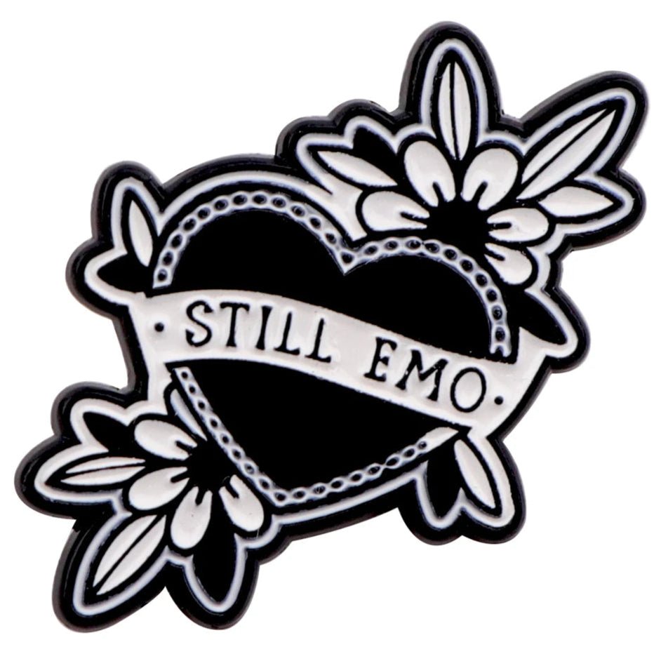 The Kiss Me Later black heart-shaped pin features white floral designs, spooky vibes, and a STILL EMO banner—perfect to pair with your favorite skeleton hand enamel pin.
