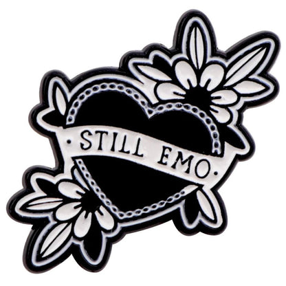 The Kiss Me Later black heart-shaped pin features white floral designs, spooky vibes, and a STILL EMO banner—perfect to pair with your favorite skeleton hand enamel pin.