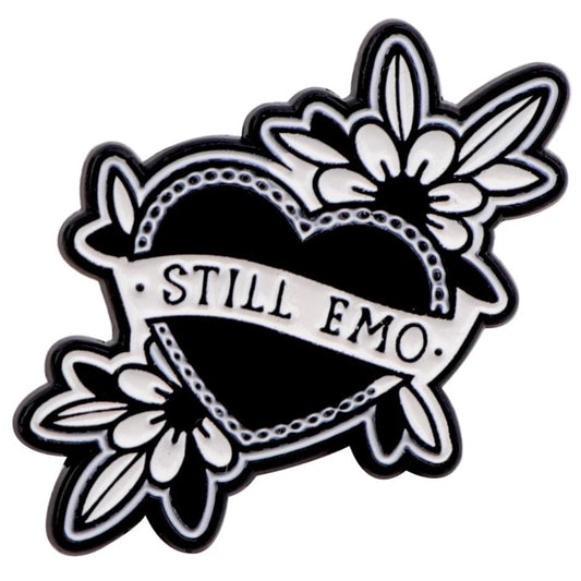 The Kiss Me Later black heart-shaped pin features white floral designs, spooky vibes, and a STILL EMO banner—perfect to pair with your favorite skeleton hand enamel pin.