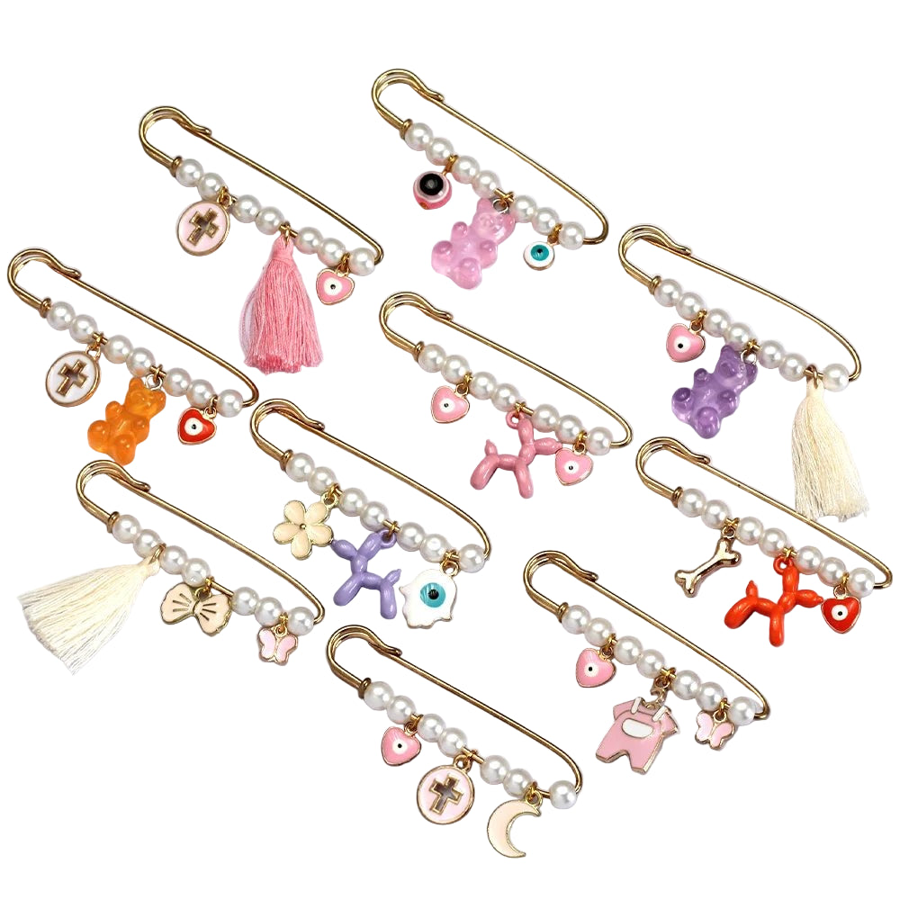 Kiss Me Later’s gold baby safety pin features pearl beads and assorted colorful charms—hearts, tassels, crosses, animals—making a charming brooch set thats a unique baby shower gift.