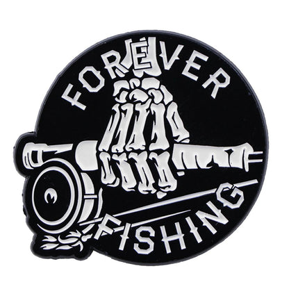 A Kiss Me Later black circular enamel pin shows a white skeleton hand holding a fishing rod, with FOREVER curved at the top and FISHING at the bottom for spooky fishing vibes.