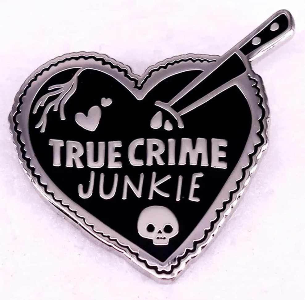 Heart-shaped red enamel pin reads TRUE CRIME JUNKIE, featuring a knife, skull, hearts, and blood drops on a black background with a silver outline.