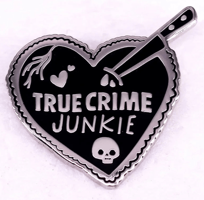 Heart-shaped red enamel pin reads TRUE CRIME JUNKIE, featuring a knife, skull, hearts, and blood drops on a black background with a silver outline.