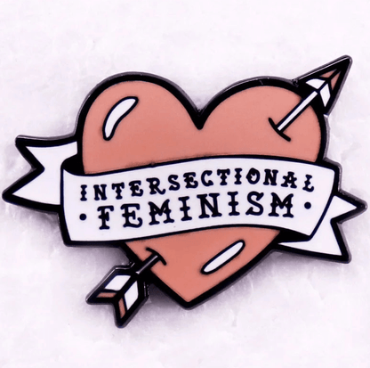 Red enamel pin features a heart with a banner reading Intersectional Feminism and an arrow piercing through. With its light pink background, this love heart pin celebrates unity and equality—perfect for your collection.