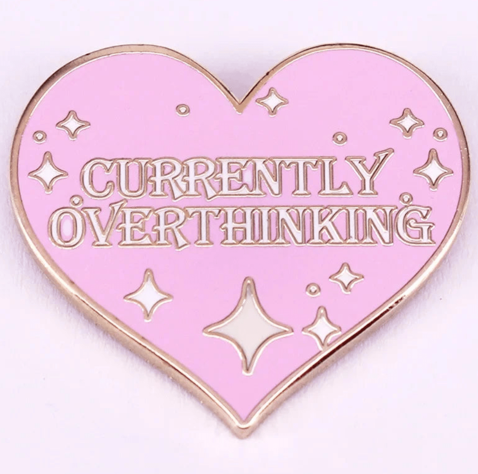 Enamel pin is pink with a heart shape, gold edges and sparkles, and features the text CURRENTLY OVERTHINKING in gold capital letters.