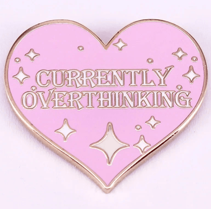 Enamel pin is pink with a heart shape, gold edges and sparkles, and features the text CURRENTLY OVERTHINKING in gold capital letters.