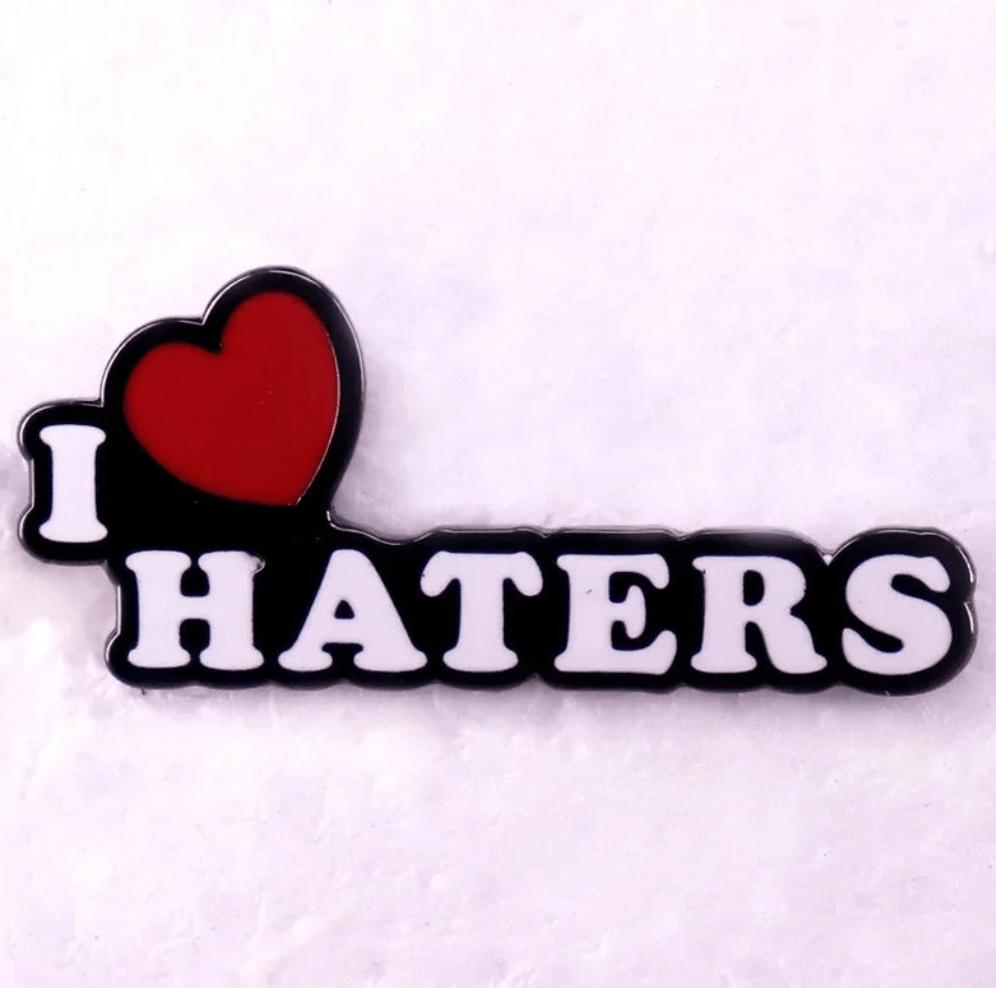 Red enamel pin features “I ♥ HATERS” in bold white letters with a heart symbol for “love,” designed against a light background.