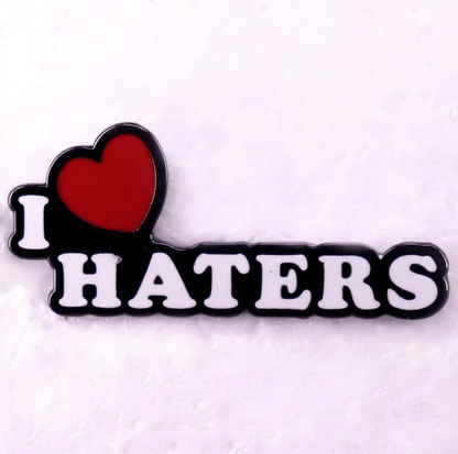 Red enamel pin features “I ♥ HATERS” in bold white letters with a heart symbol for “love,” designed against a light background.