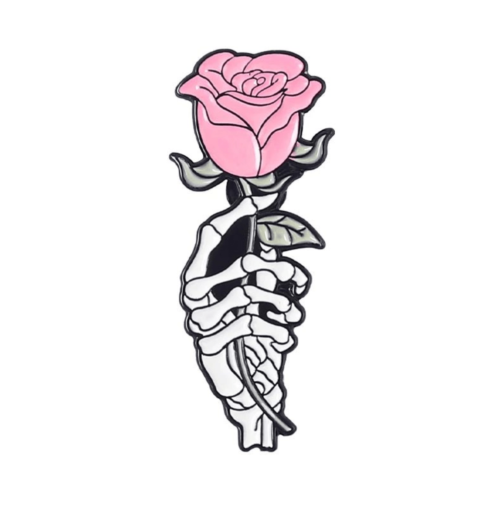 A skeleton hand holds a pink rose with green leaves on a white background—an ideal enamel pin design 