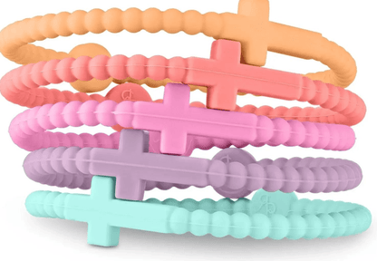 Five textured, non-toxic silicone Cutie Bracelets by Kiss Me Later in pastel orange, coral, pink, purple, and mint are stacked together. Each features a raised cross detail and a small round accent.