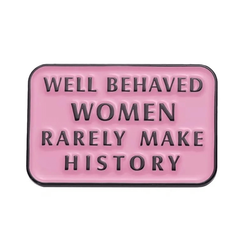 A rectangular pink sign with black raised letters stating WELL BEHAVED WOMEN RARELY MAKE HISTORY, inspired by the iconic enamel pin and badge.